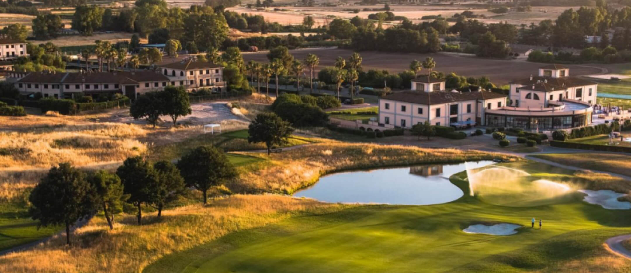 Sunset-lit golf course with manicured greens, sand bunkers, and a tranquil pond