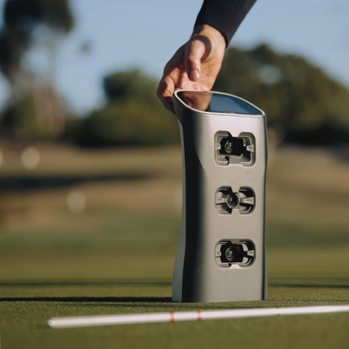 Hand holding gray rectangular launch monitor Spica 3 on golf green