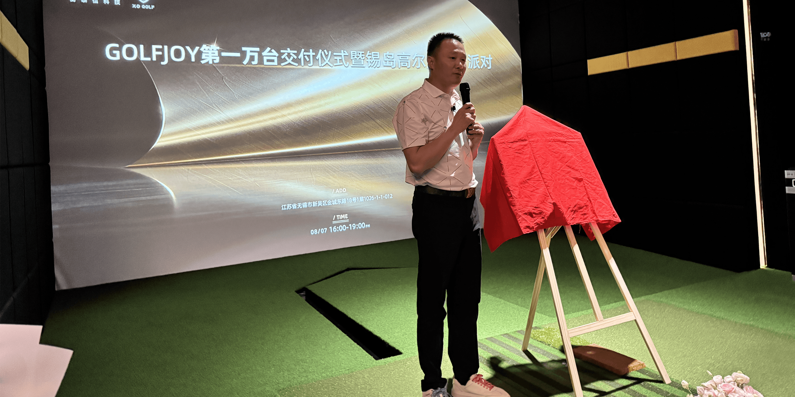 Man standing in front of a screen with 'GOLFJOY' branding, holding a microphone