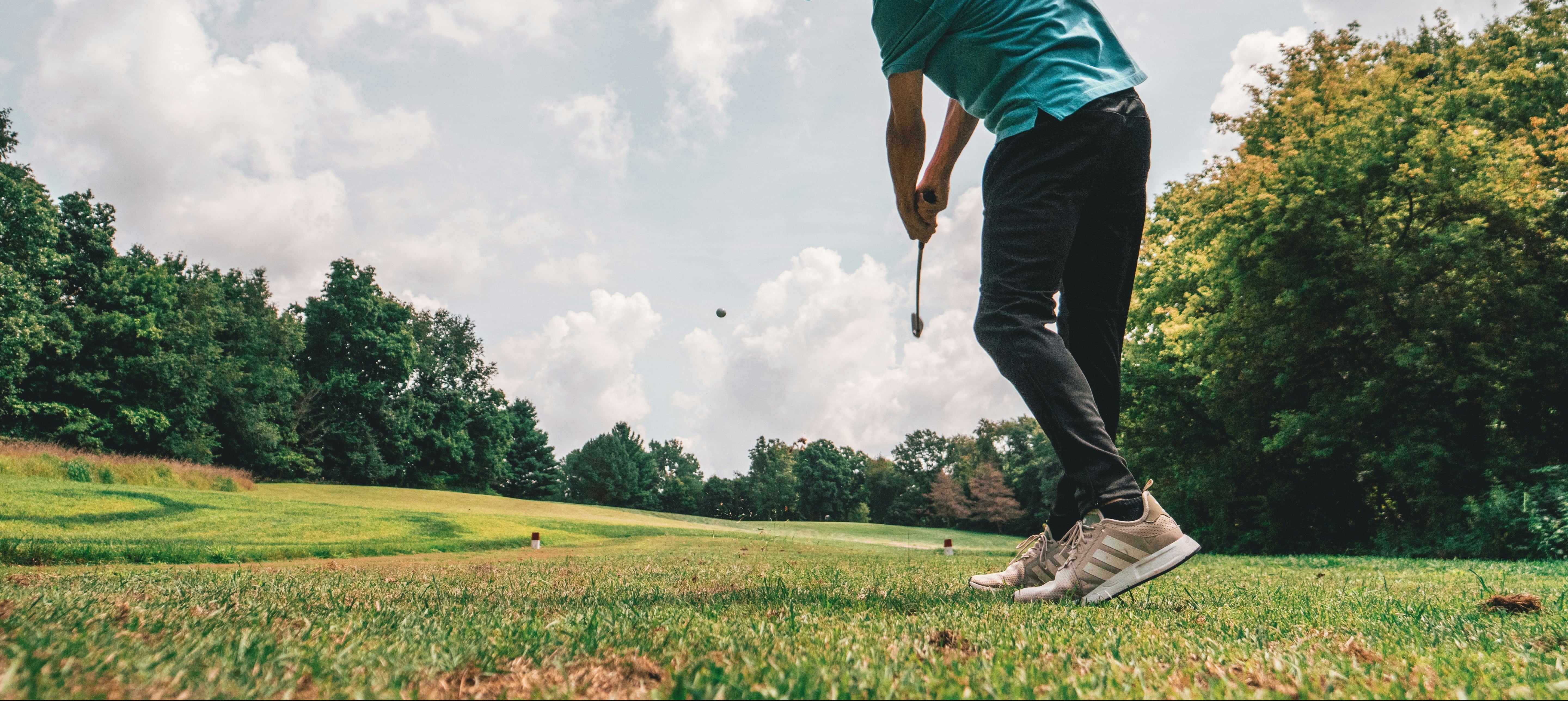 Golfer in action on a golf course with trees and sky in the background